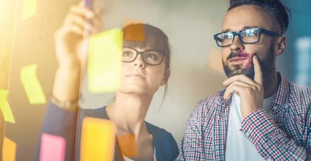 male and female adults looking at post it notes on a board