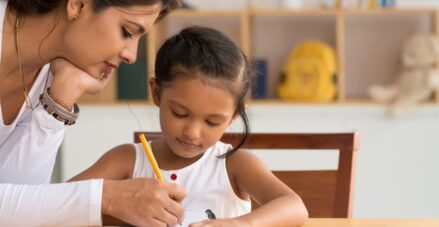 Female adult teacher helping a young female student write in a school planner