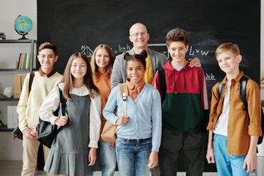 group of students smiling with their teacher in front of a chalkboard with a math problem