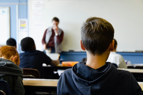 view from the back of a classroom with students watching teacher
