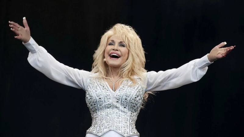 Dolly Parton in a white dress smiling and holding arms open